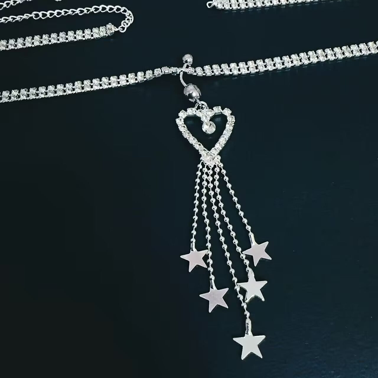 Close up detail of rhinestone heart pendant with falling star tassels on belly button ring waist chain.