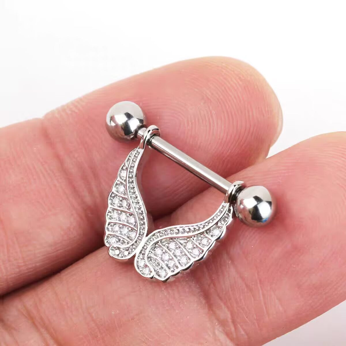 Close-up of a person holding a sparkling silver angel wings nipple shield to show size and crystal detail.