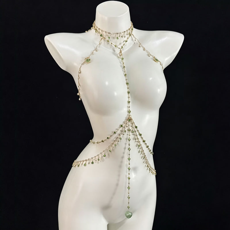 A complete full-body view of an intricate silver body chain harness adorned with numerous peridot green crystals and a large dangling heart-shaped crystal on a white female mannequin.
