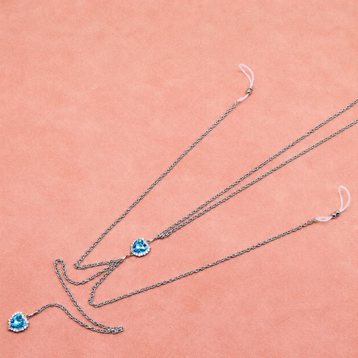 Lake blue heart nipple chain laid diagonally on peach fabric with two silicone loops and draped chains
