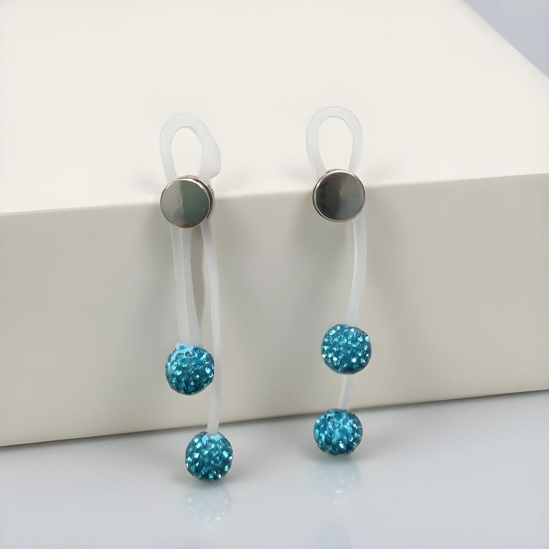 Pair of lake-blue nipple clips displayed over a cream block with translucent straps and blue bead drops.