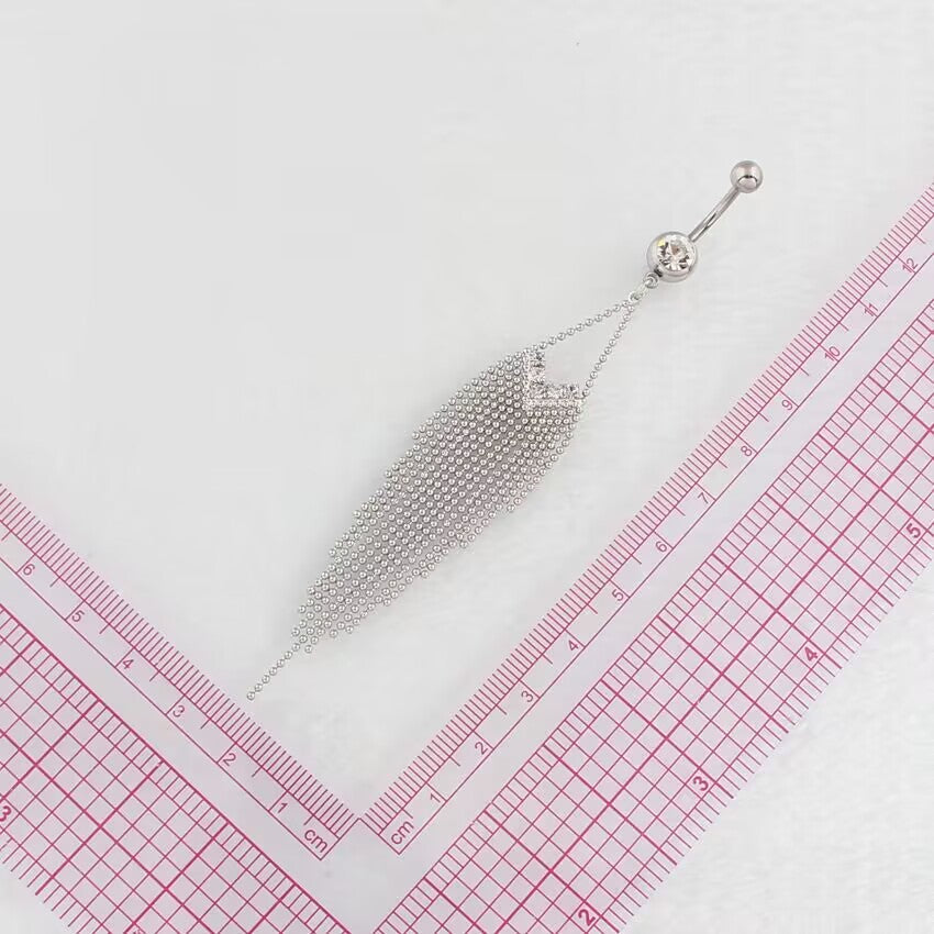 Silver dangle tassel belly button ring placed next to a pink grid ruler to show precise sizing and elongated fringe length for body piercing placement.