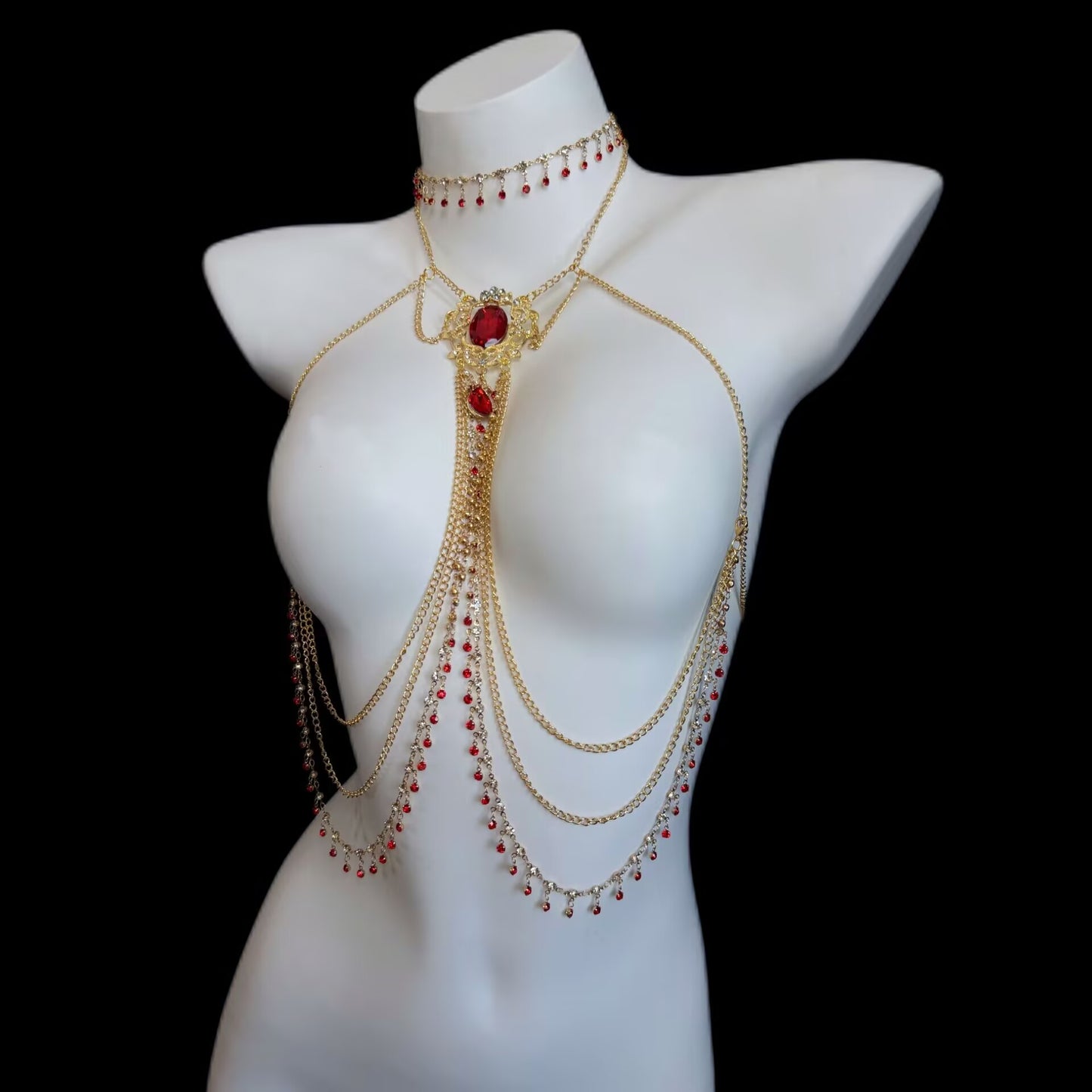 Luxurious gothic multi-tier chest body chain and choker necklace set adorned with ruby red rhinestones and gold dangling tassels on a white mannequin torso.
