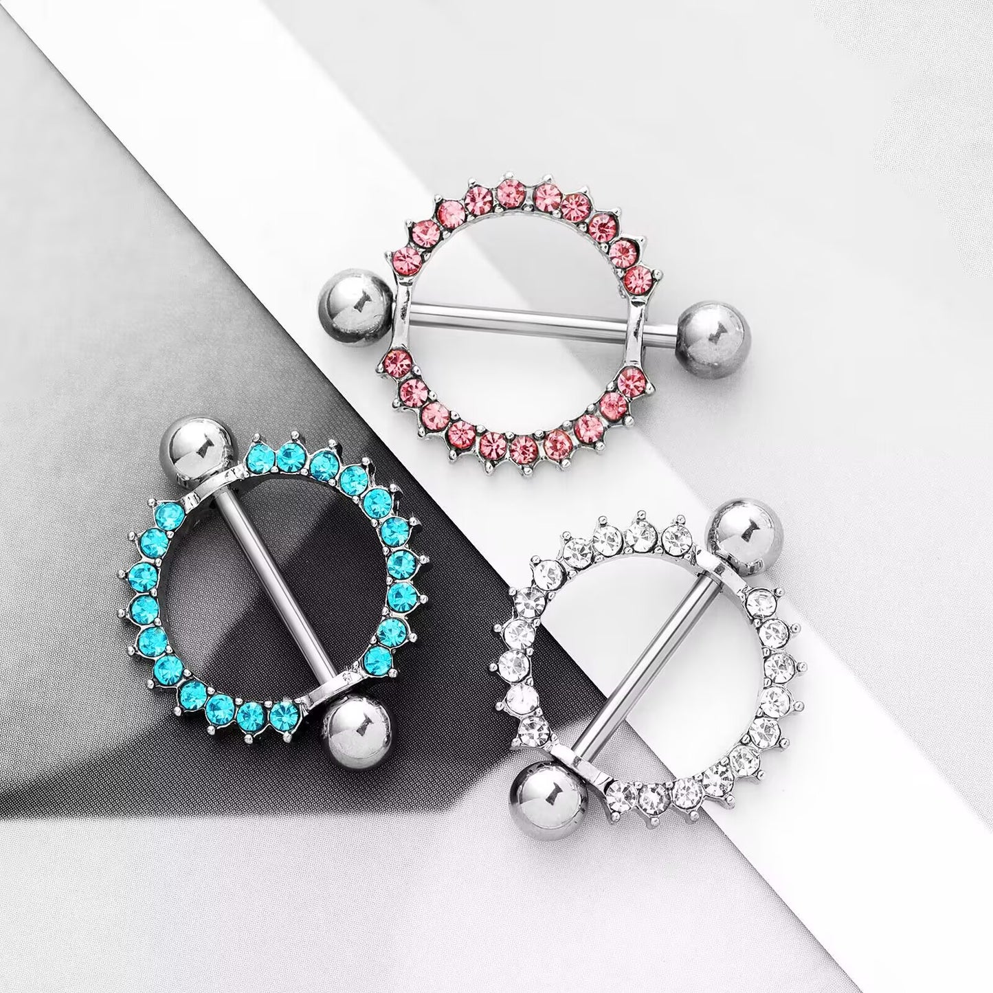 Real product shot of shiny 14G crystal nipple rings in clear, blue, and pink colors, highlighting the textured design and glamorous shine.
