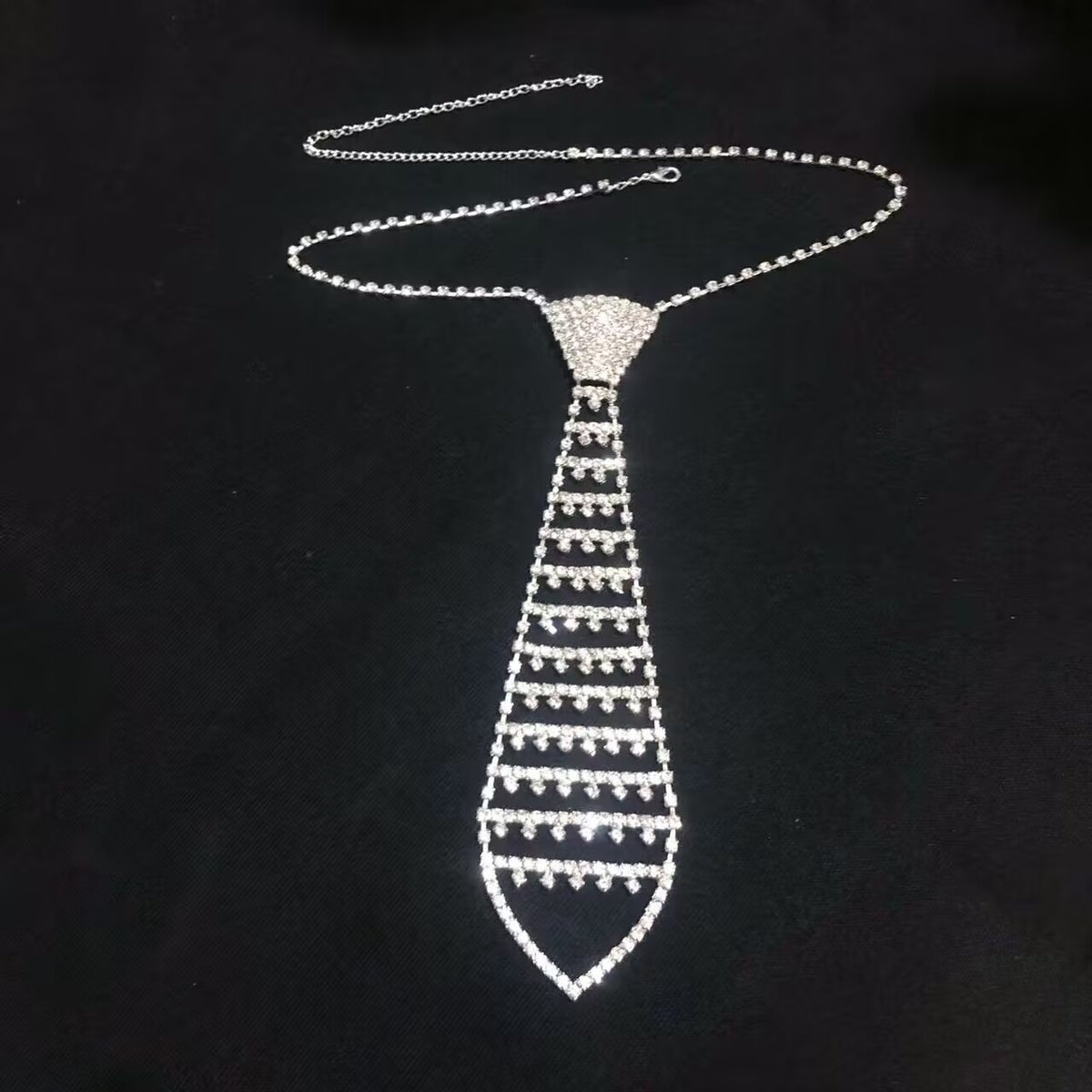 Tapered grid mesh crystal tie choker body jewelry piece lying flat on black background.