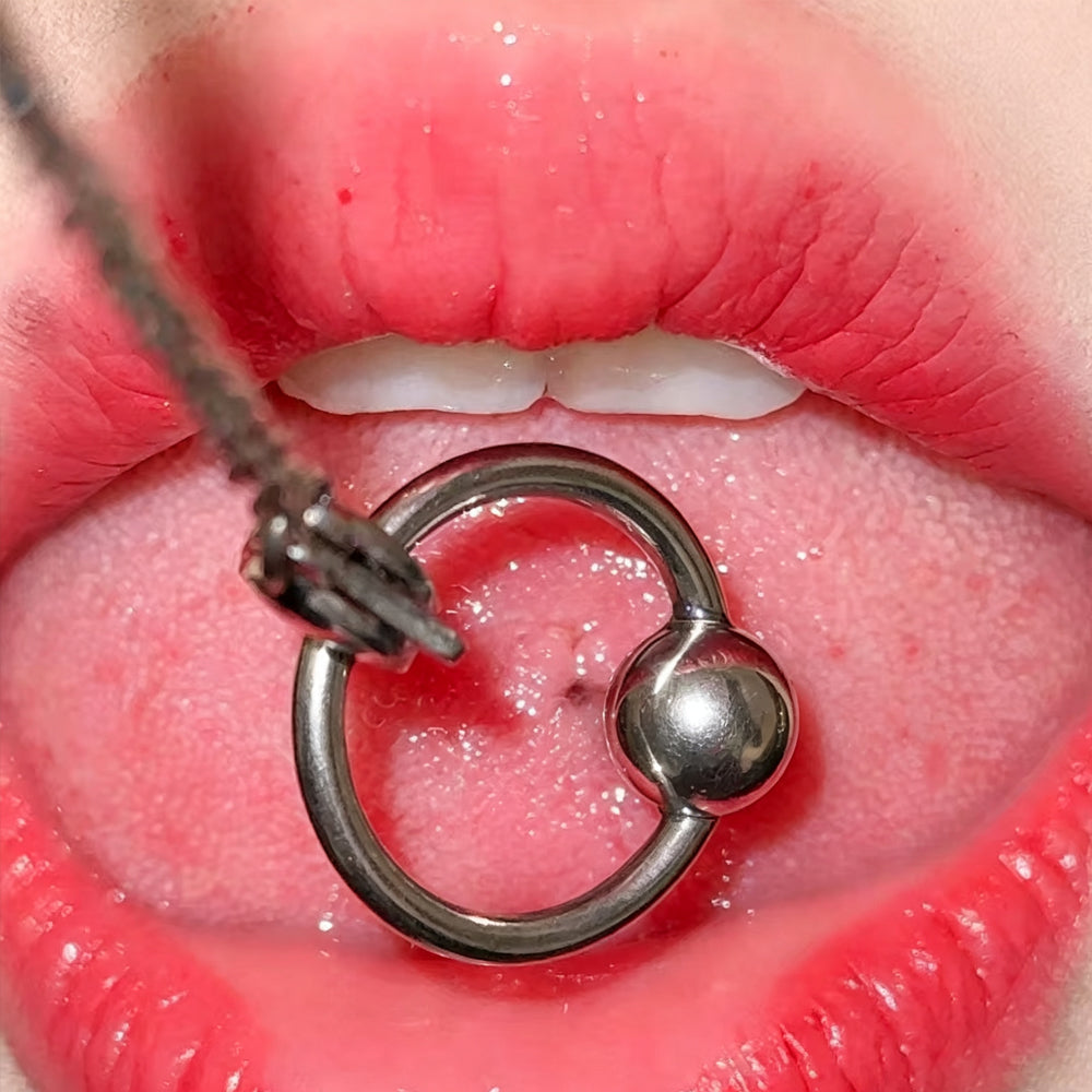 Extreme close-up of a high-polish 14G stainless steel tongue barbell with a free-moving slave ring on the center of the tongue.