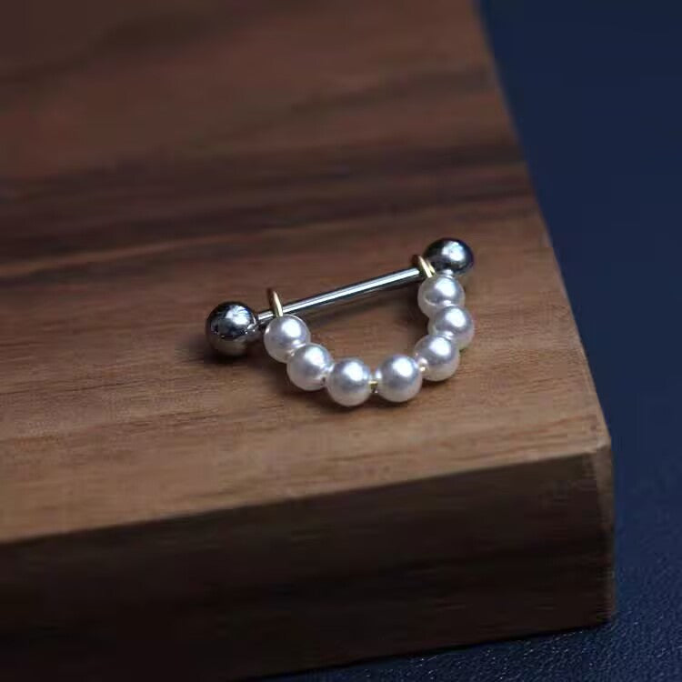 Minimalist white pearl shield nipple barbell body piercing ring on wooden base.