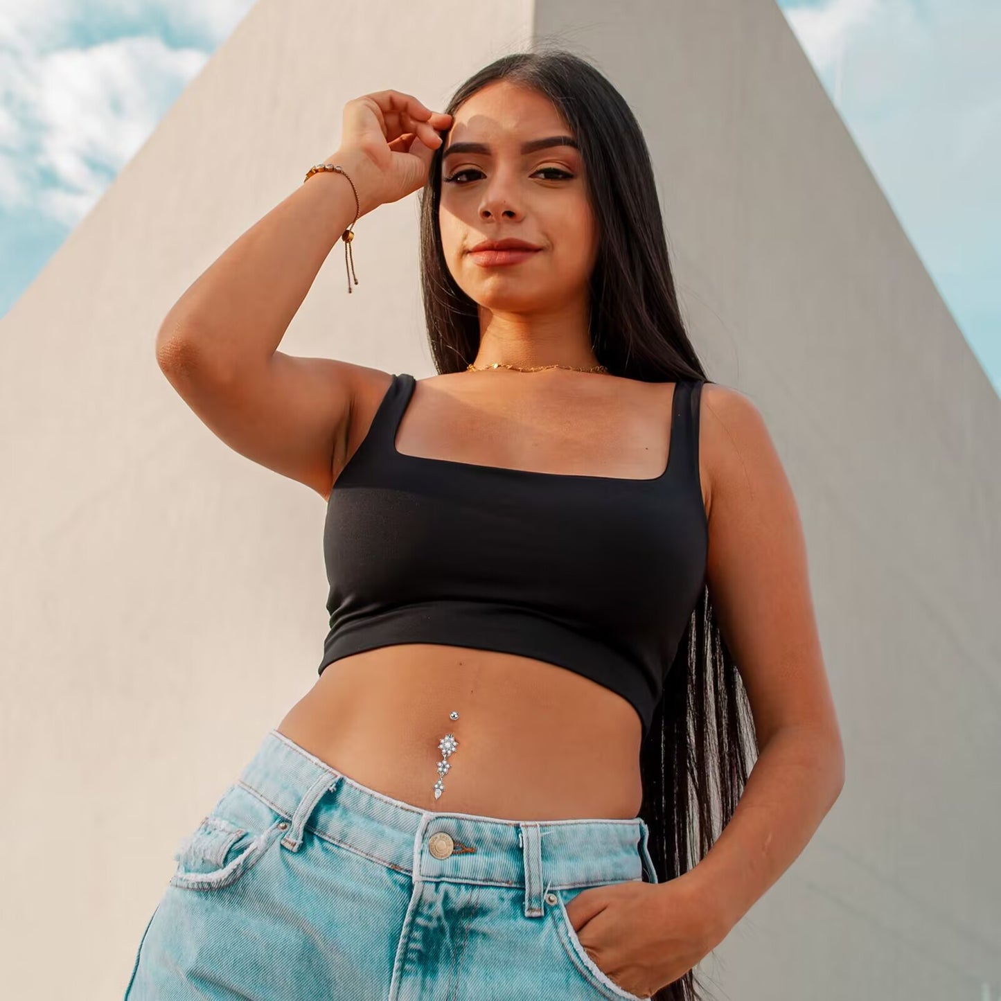 Woman wearing a sparkling crystal dangle navel ring paired with high-waisted jeans and crop top for beach fashion.
