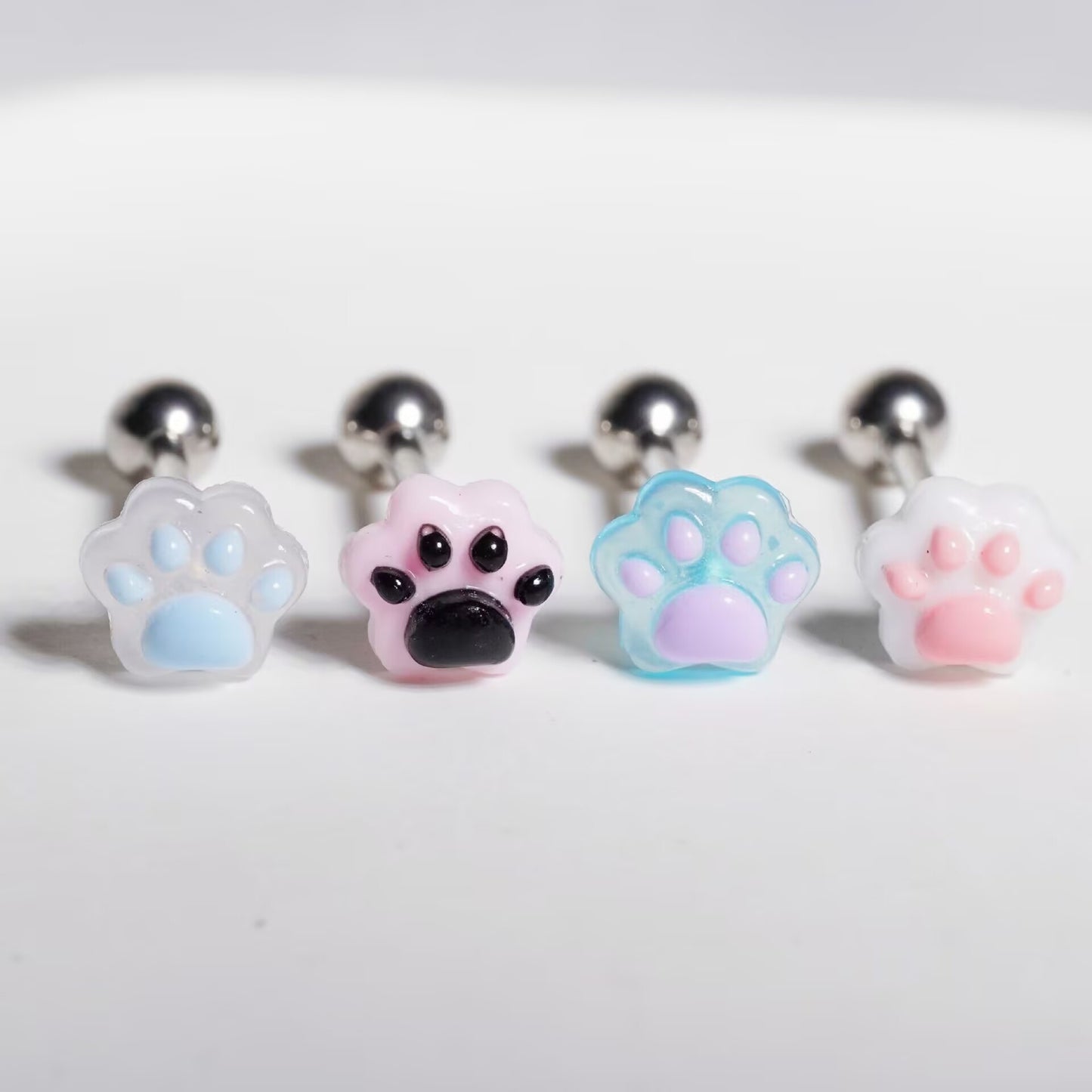 Four different colored resin cat paw tongue barbells including blue, pink, lavender, and white