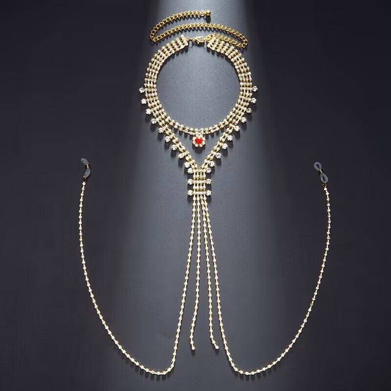 Flat lay of an integrated rhinestone choker harness with red center gem and dangle non-pierced nipple chains against a dark background.