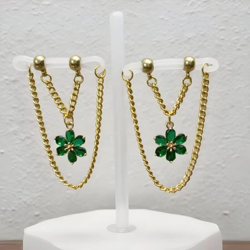 Non-pierced nipple jewelry displayed on clear loops with green crystal flower charms and gold drop chains.