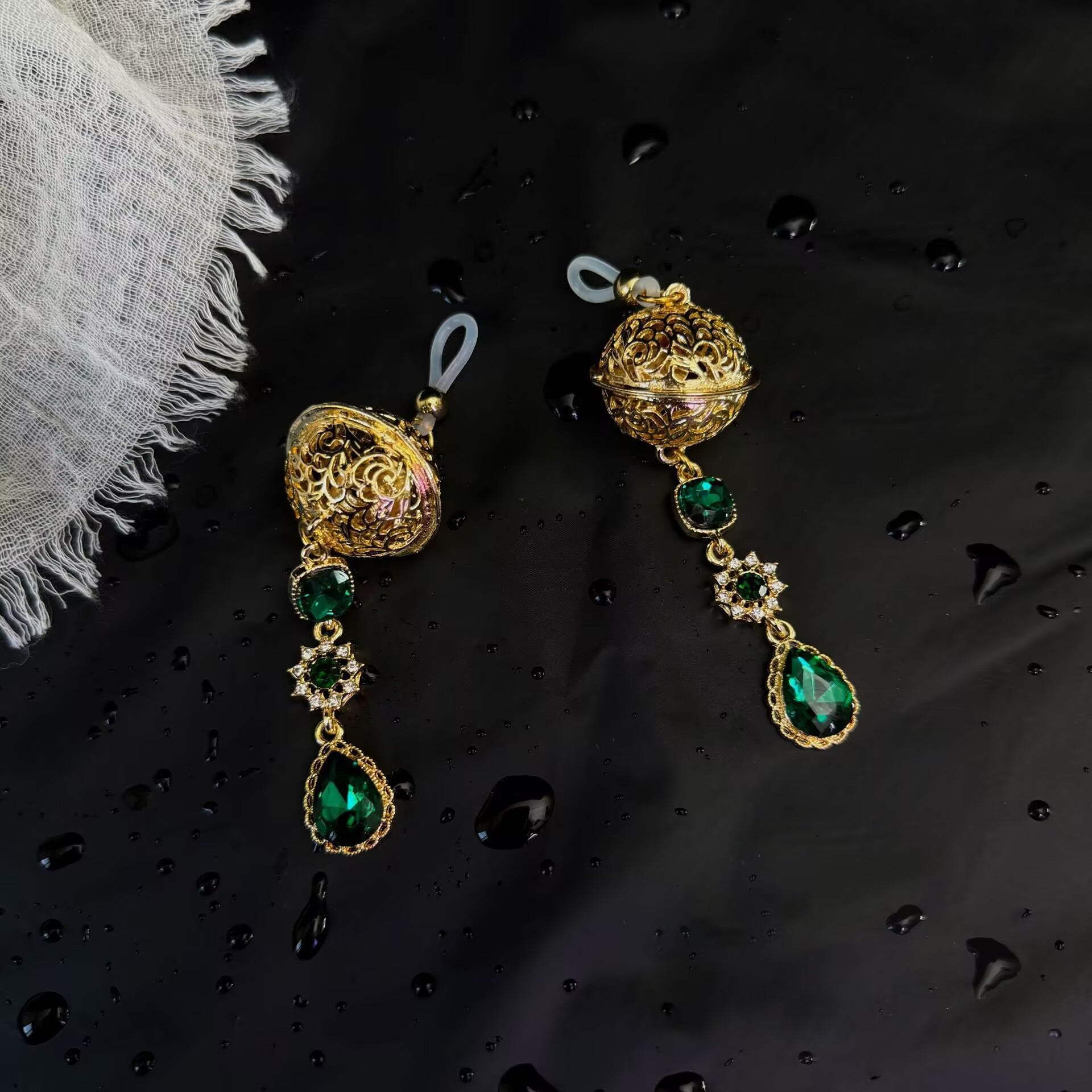 Front view of gold filigree sphere non-pierced nipple clamps with silicone loops and teardrop emerald crystals on dark background.