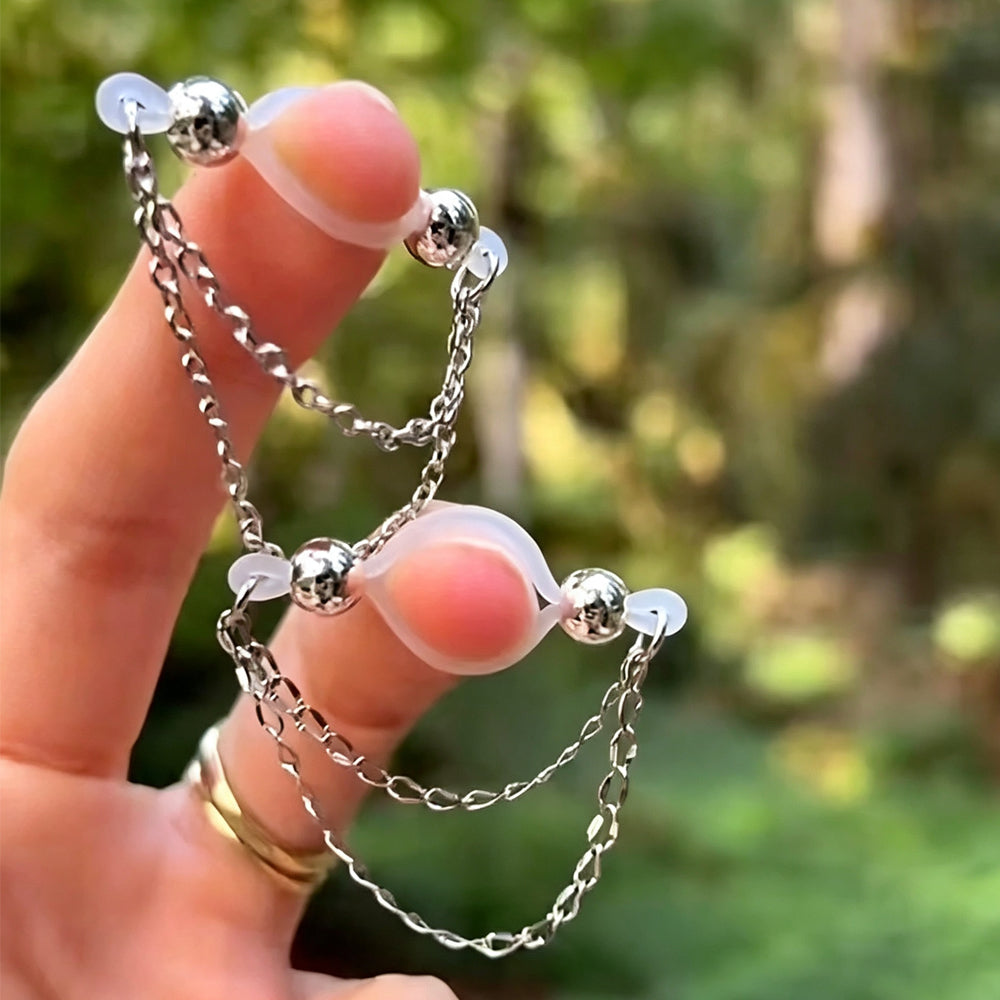 Hand holding a pair of adjustable clear silicone non-piercing nipple clamps with double hanging silver chains.
