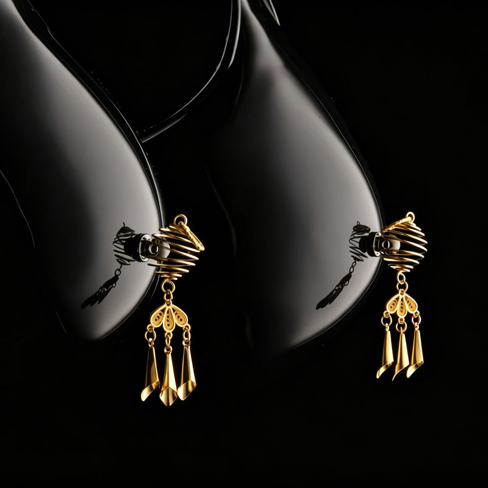 Close-up of a model wearing gold non-piercing nipple dangles against a dark aesthetic background.