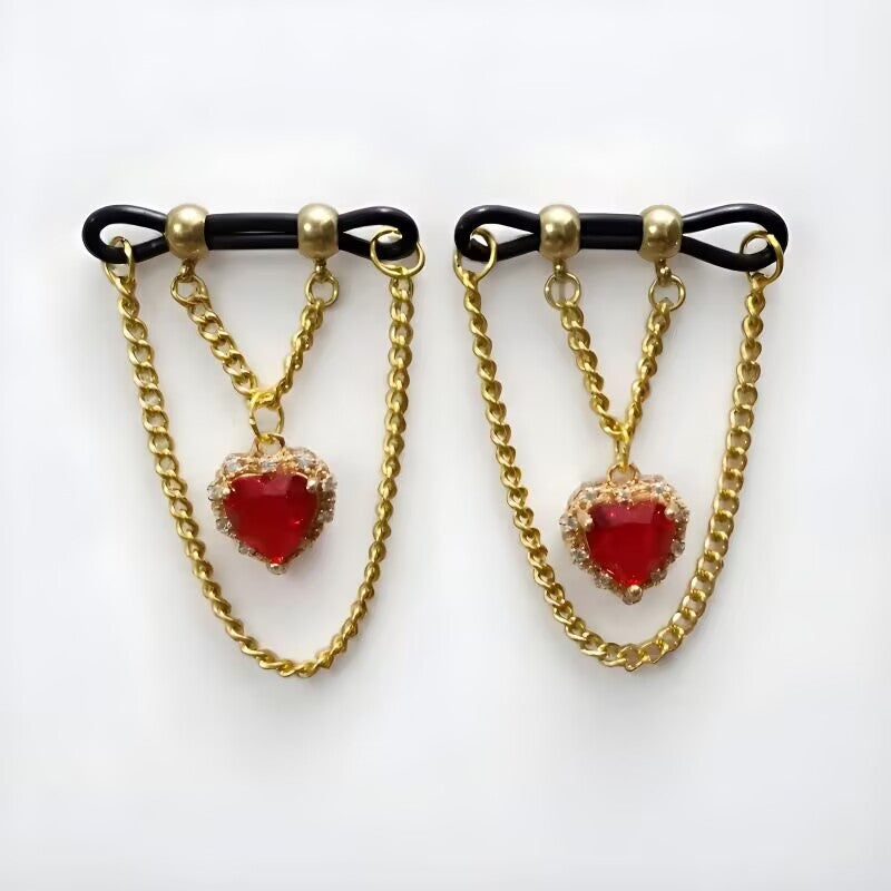 Non piercing nipple rings featuring red heart crystal dangles and double layer gold chains on adjustable black loops, sold as a pair.