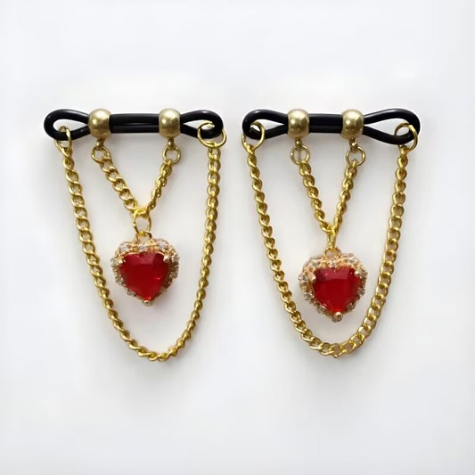 Non piercing nipple rings featuring red heart crystal dangles and double layer gold chains on adjustable black loops, sold as a pair.