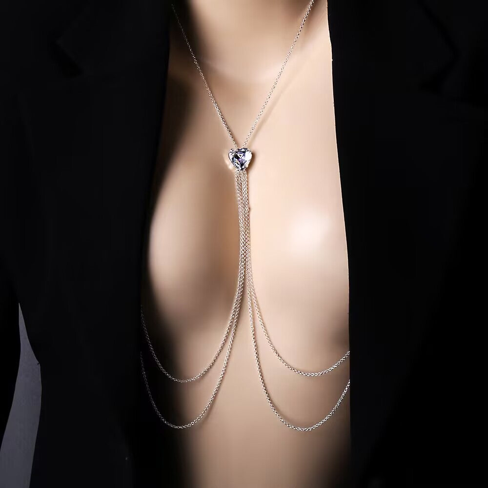 A close-up of a model wearing a non-piercing white crystal heart nipple chain body jewelry underneath a black open blazer, showcasing the multi-layer silver tassel harness over the chest.