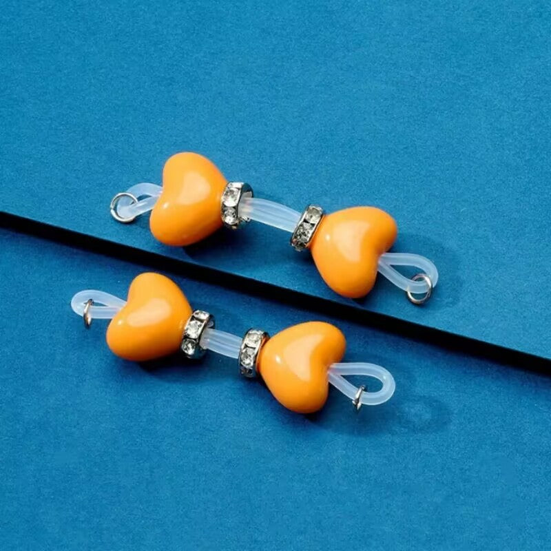 Pair of bright orange heart non-piercing fake nipple rings crafted with clear elastic silicone and silver rhinestone spacers.