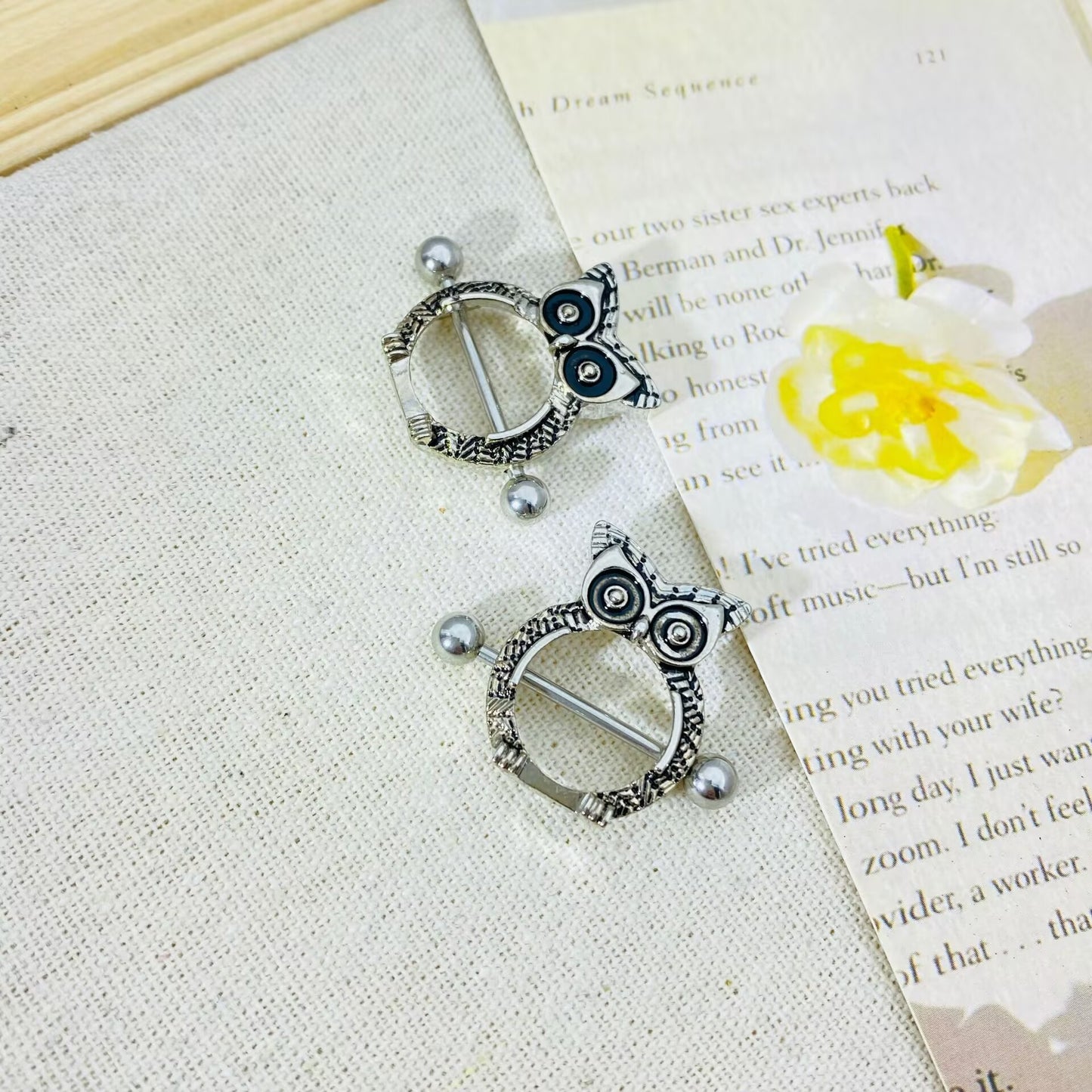 Close-up of owl nipple rings displayed on a decorative paper and flower background.