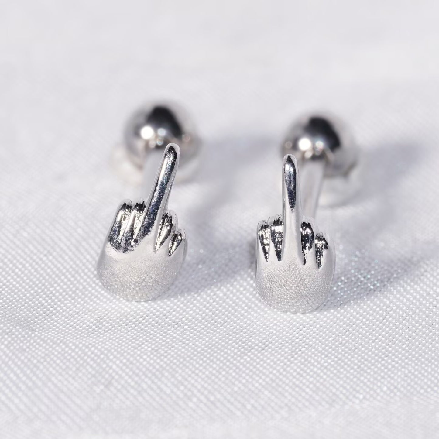 Pair of middle finger barbell studs displayed on white fabric background.