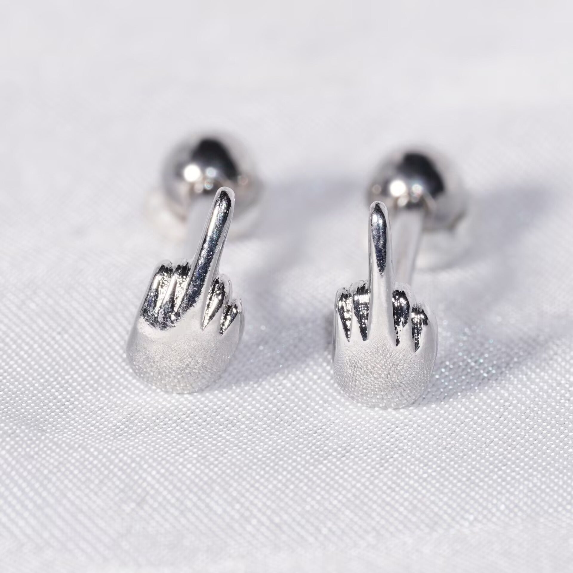 Pair of middle finger barbell studs displayed on white fabric background.