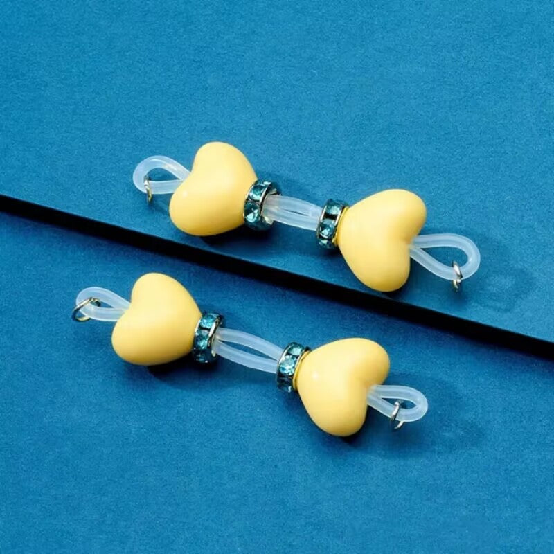 Pair of pastel yellow heart silicone fake nipple jewelry pieces with teal rhinestone rings for a playful look.