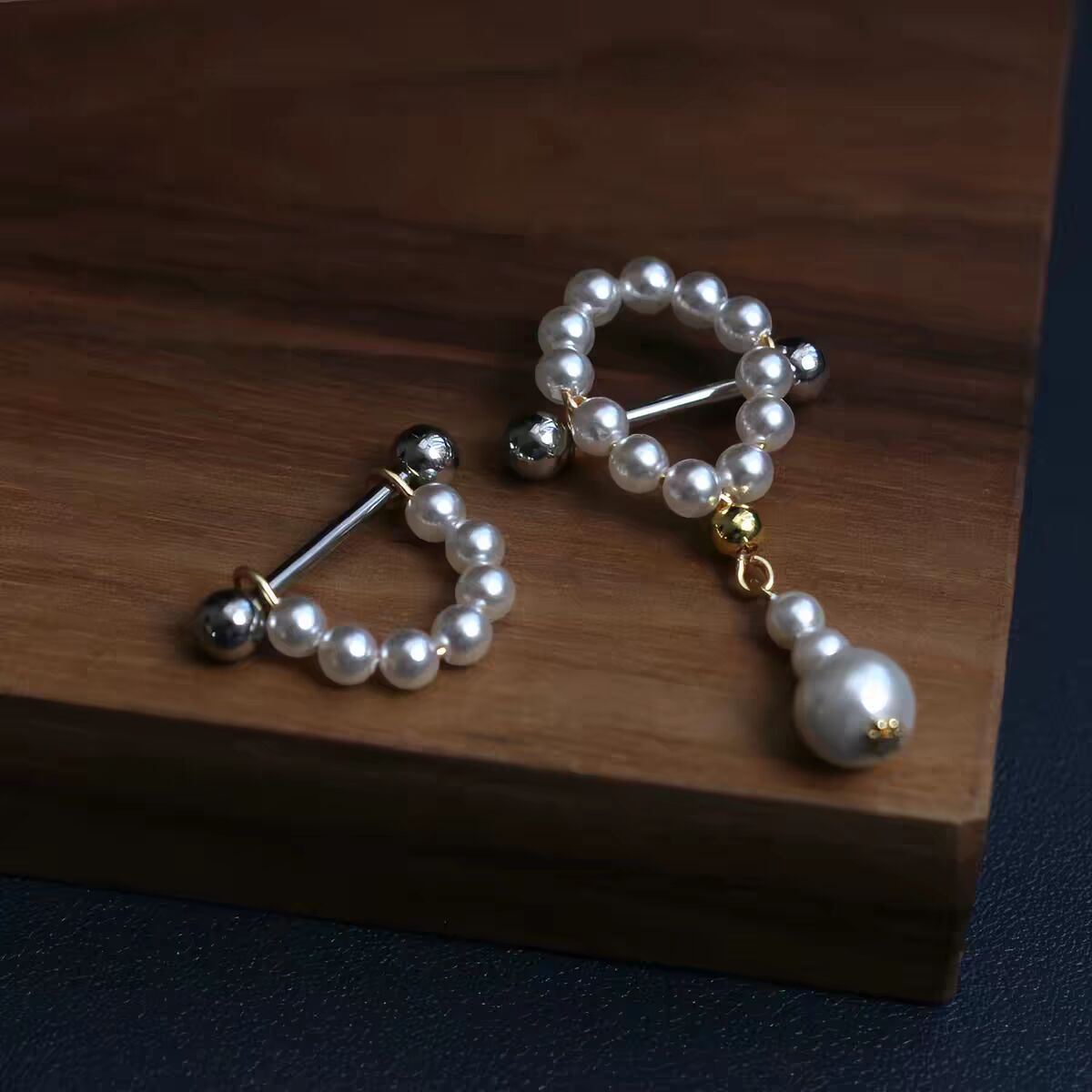 Pair of white pearl nipple jewelry featuring one dangle barbell and one shield barbell for body piercing.