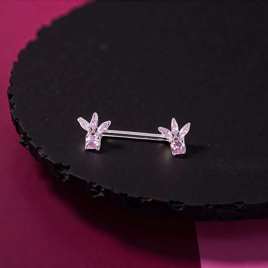 Close-up side view of a pink floral crown nipple barbell featuring sparkling marquise gems on a minimalist black stand.