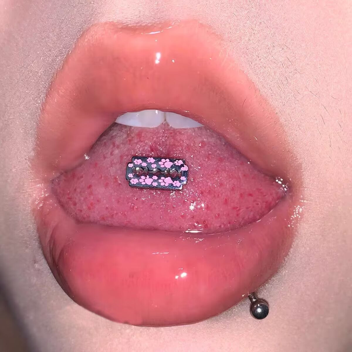 Person wearing a pink paw print razor blade tongue ring barbell
