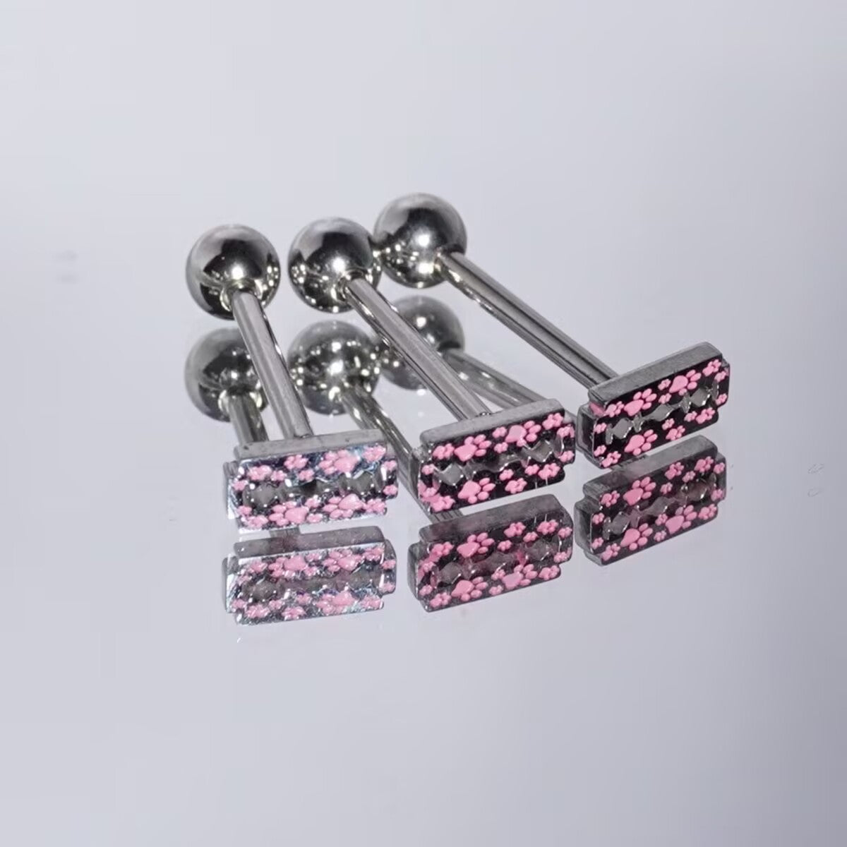 Three pink paw print razor blade tongue rings on a reflective mirror background