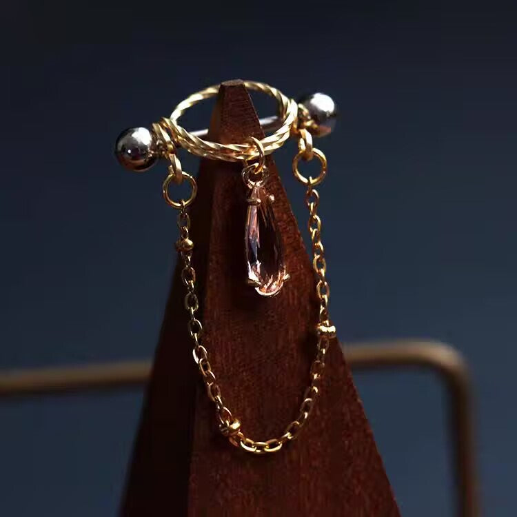 Light pink rose waterdrop CZ nipple shield ring with delicate side chain accent on wooden display.