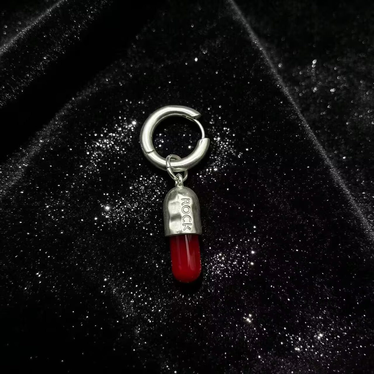Punk rock capsule drop hoop earring on a black sparkling velvet background.