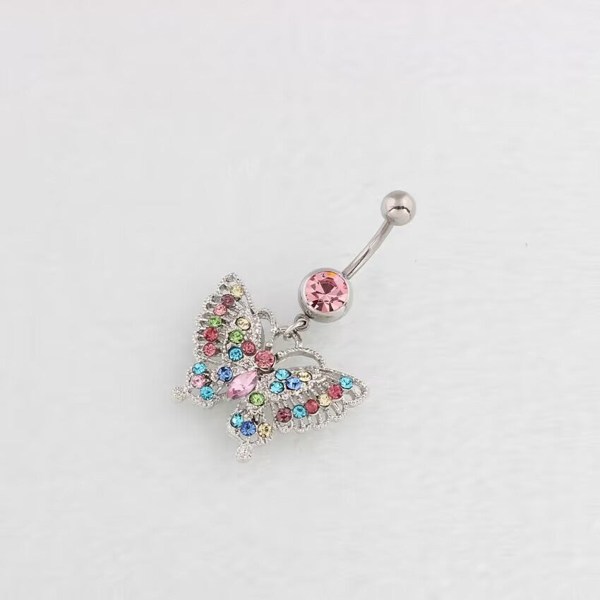 Angled flat lay view of a multi-color crystal butterfly dangling belly ring with a pink crystal accent on a smooth white surface.