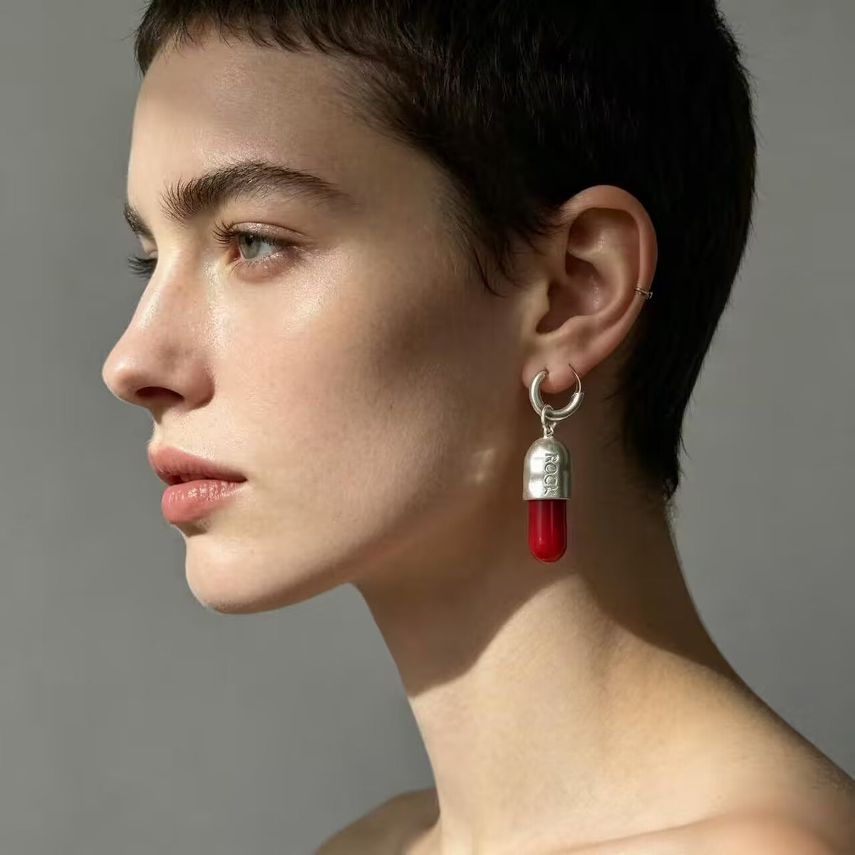 Model wearing red pill dangle hoop earring with rock engraving in gothic style.