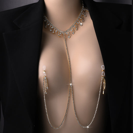 A close-up of a model wearing a sparkling gold rhinestone choker necklace connected to non-pierced nipple clamps with hanging tassels, layered under a black blazer as statement festival body jewelry.