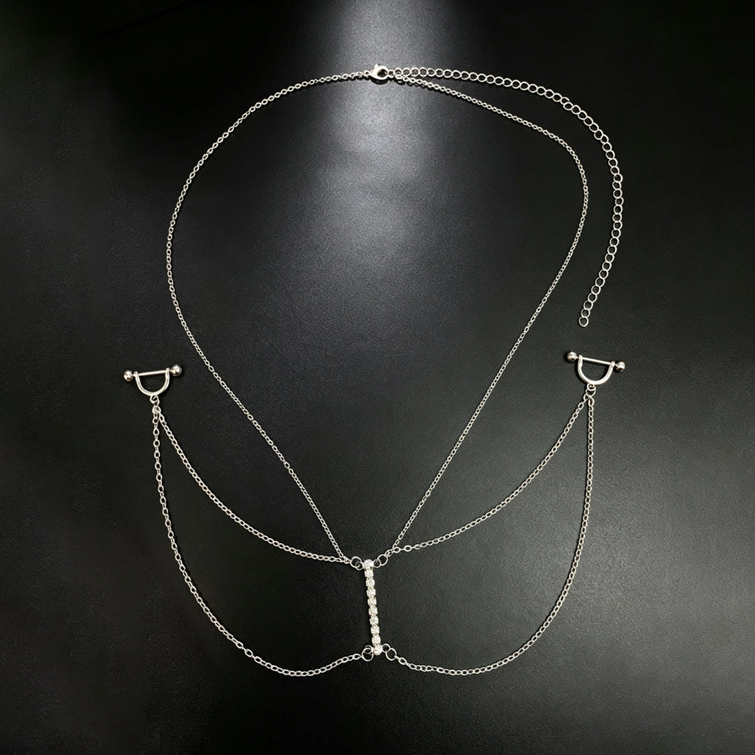 All-in-one silver nipple piercing body chain harness featuring a necklace chain and a central vertical row of sparkling rhinestones on a black background.