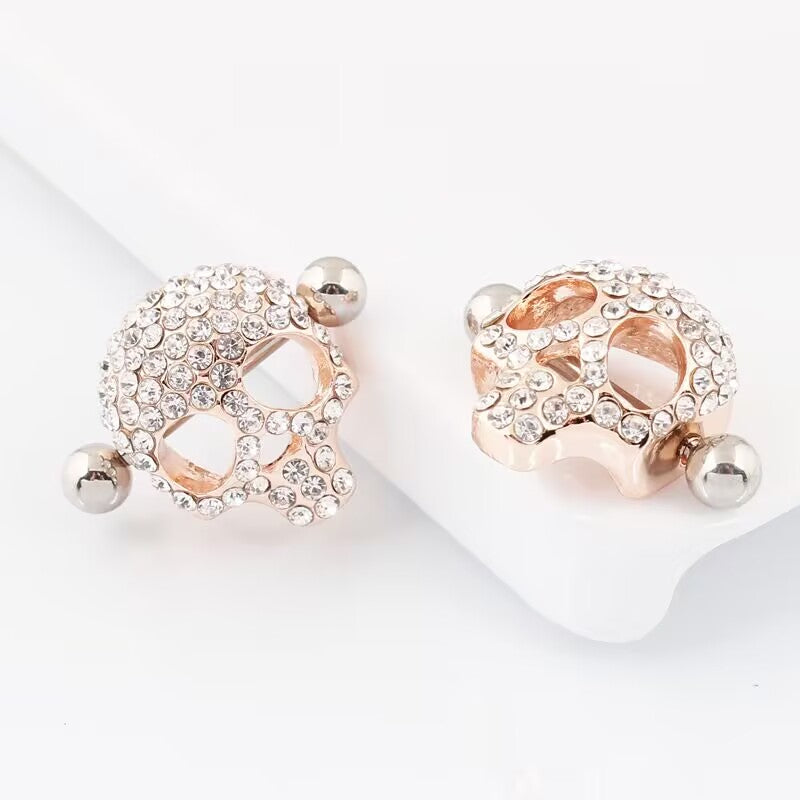 Two rose gold skull nipple shields encrusted with clear crystals on a clean white surface.