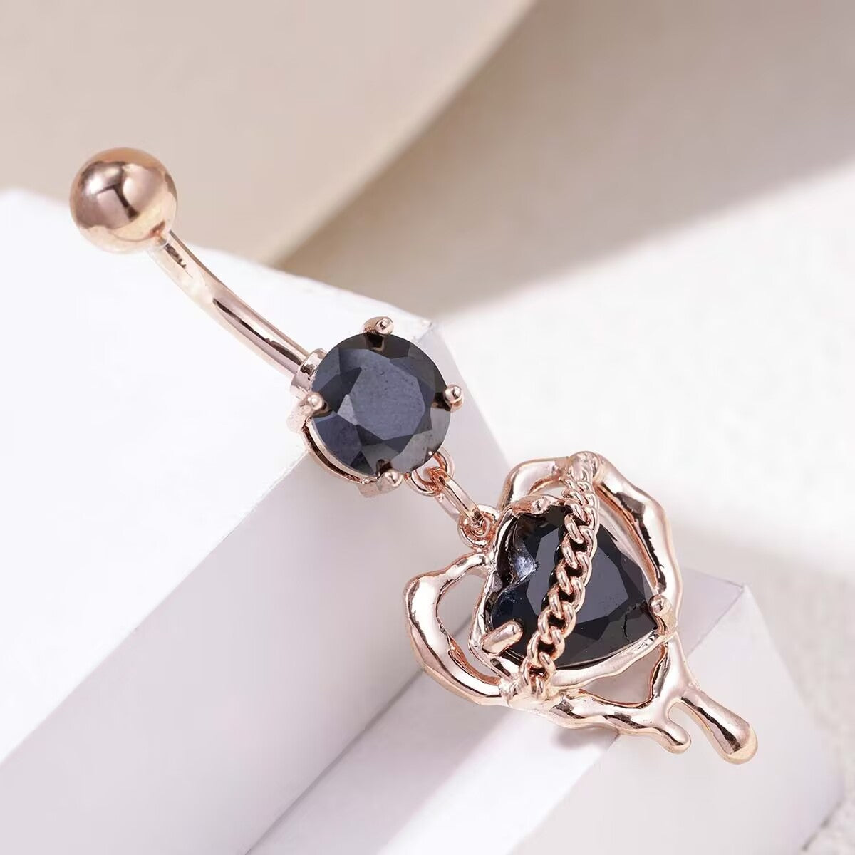 Close up of rose gold liquid lava black heart dangle belly jewelry resting on white pedestal