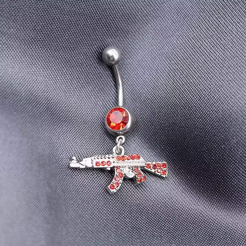 Close-up of a silver belly button ring featuring a large ruby red top crystal and matching red stone paved AK47 charm.