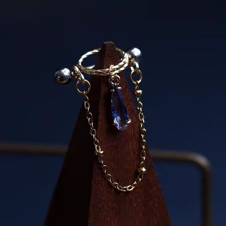 Royal sapphire blue pear-cut CZ dangle nipple shield barbell with cascading gold chain.