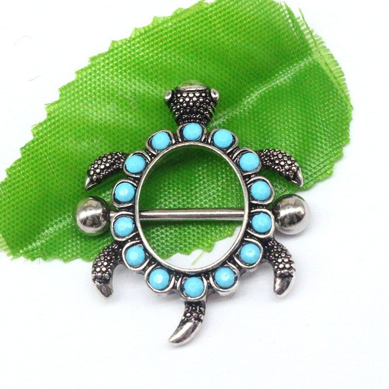 Unique turtle-shaped nipple ring with blue stones resting on a green leaf background.
