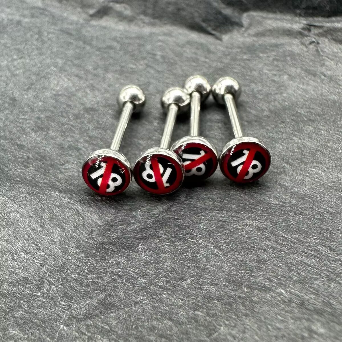 Set of four 18+ sign flat disc tongue rings displayed on a dark slate texture.
