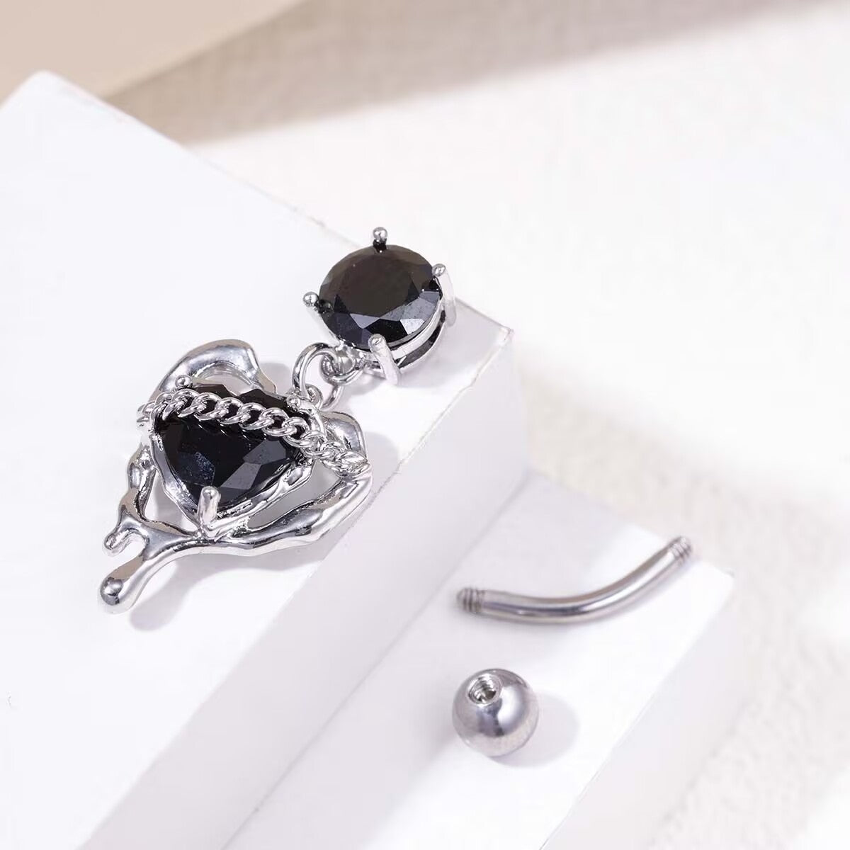 Silver curved barbell navel piercing jewelry with detached black heart molten lava dangle component