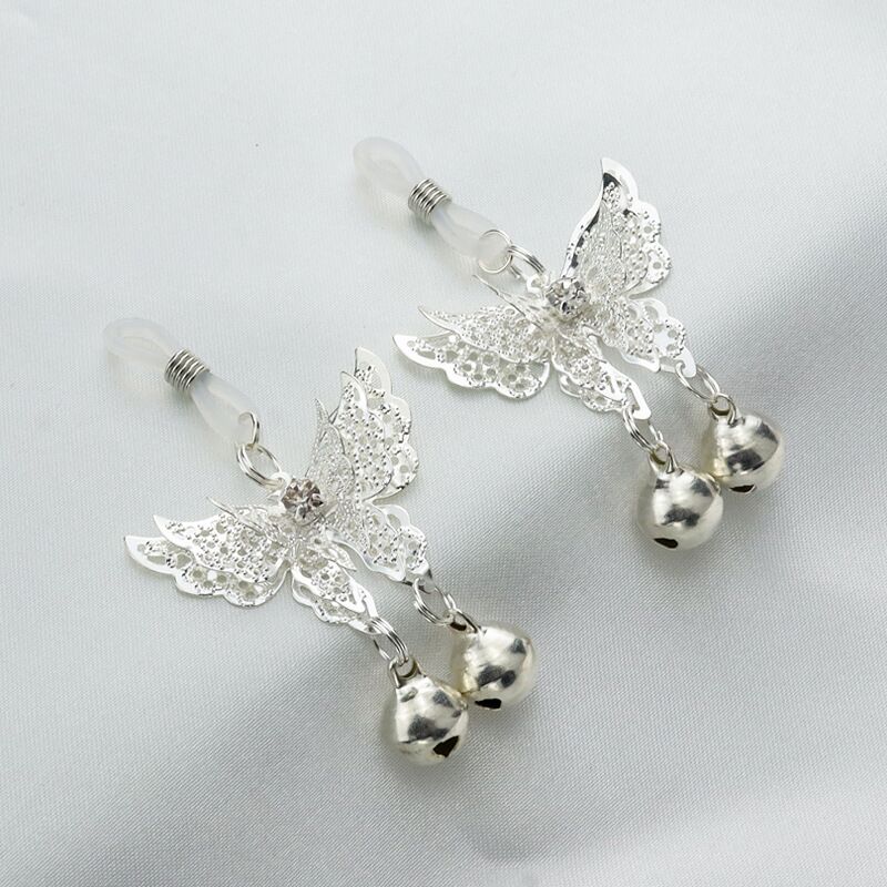 Two elegant butterfly-shaped intimate rings with jingling bells resting on a soft grey fabric surface.