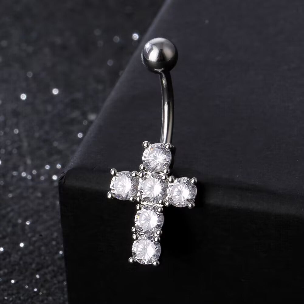 Close-up view of a sparkling silver CZ cross navel ring displayed on dark background for Y2K style.