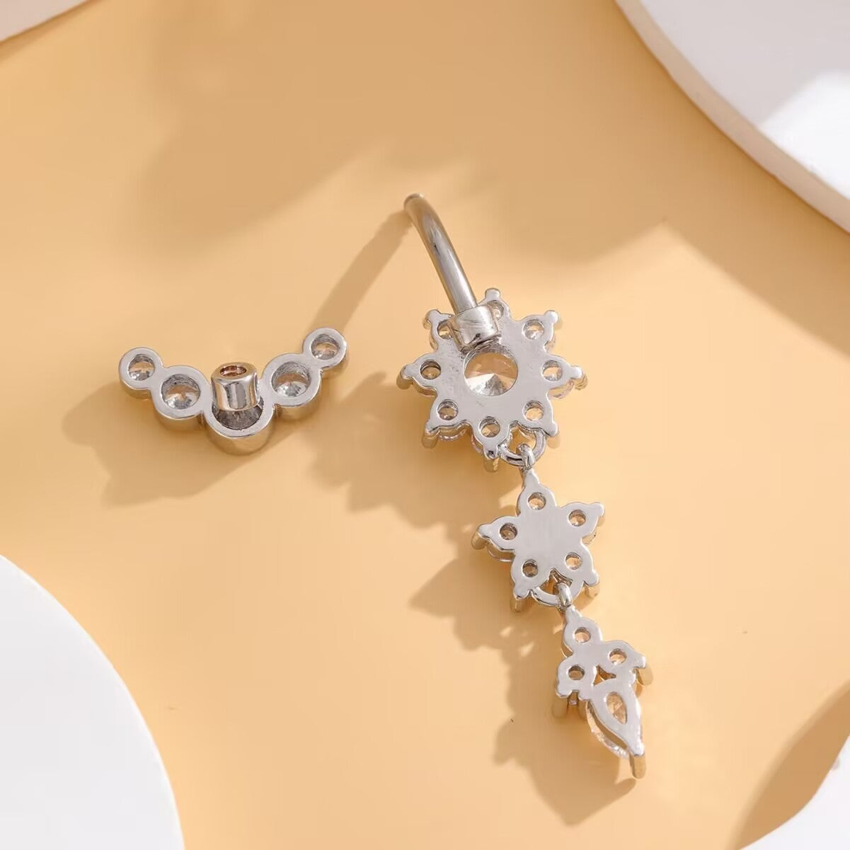 Silver dangle navel ring detached showing top curved zircon top and threaded curved bar component.