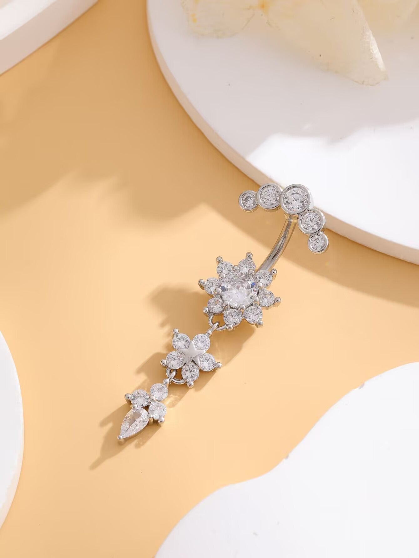 Overhead view of silver floral dangle belly ring with cascading crystal charms on neutral background.