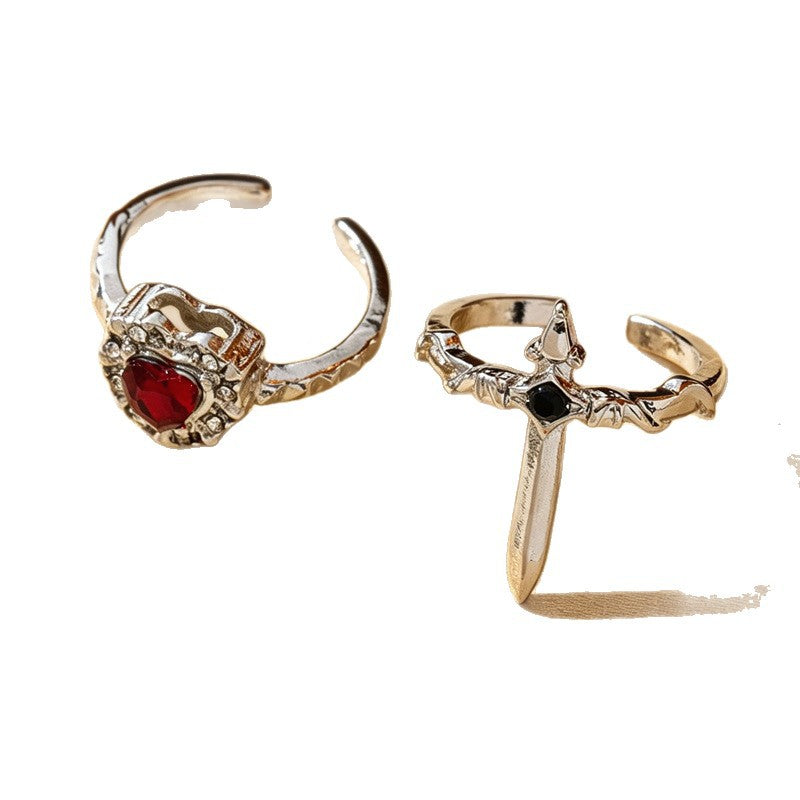 One silver-tone red heart open ring beside one sword open ring on a white background