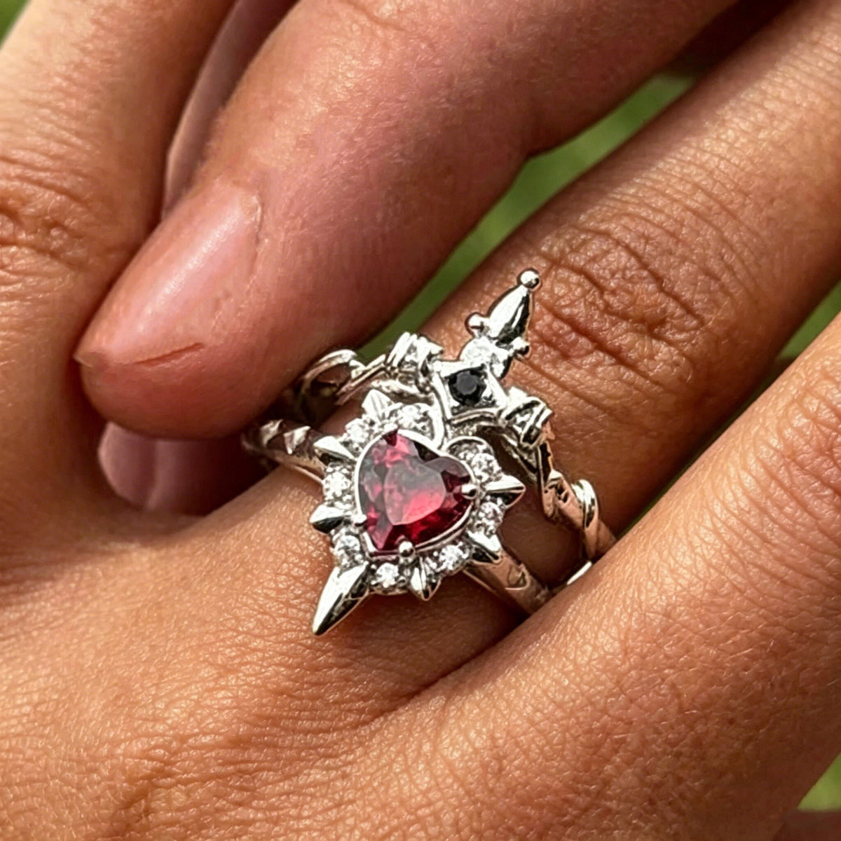 One silver-tone red heart ring stacked with one sword ring on a finger