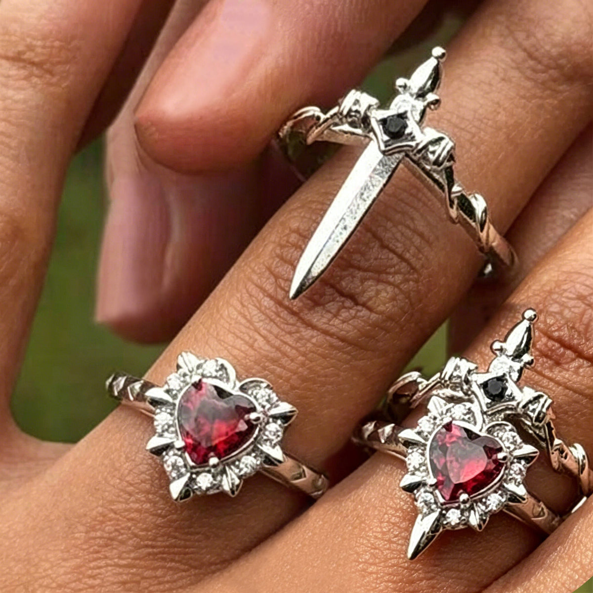 Silver-tone heart and sword rings worn separately and stacked on fingers, with red heart stones